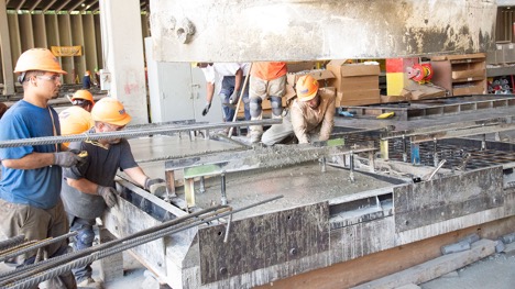 A group of fabricators casting concrete into steel formwork.